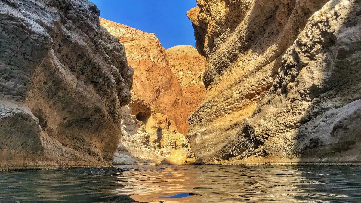Narrow sandstone walls closing over dark still water where the Wadi Shab swim begins