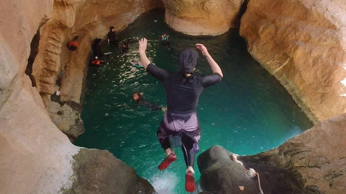 A man jumping from a ledge into a round turquoise pool below the canyon rock