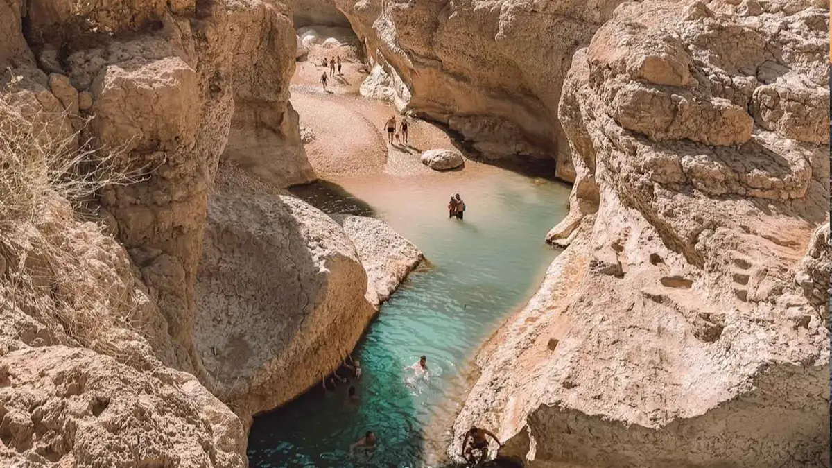 Swimmers in a turquoise channel between sandstone boulders in Wadi Shab