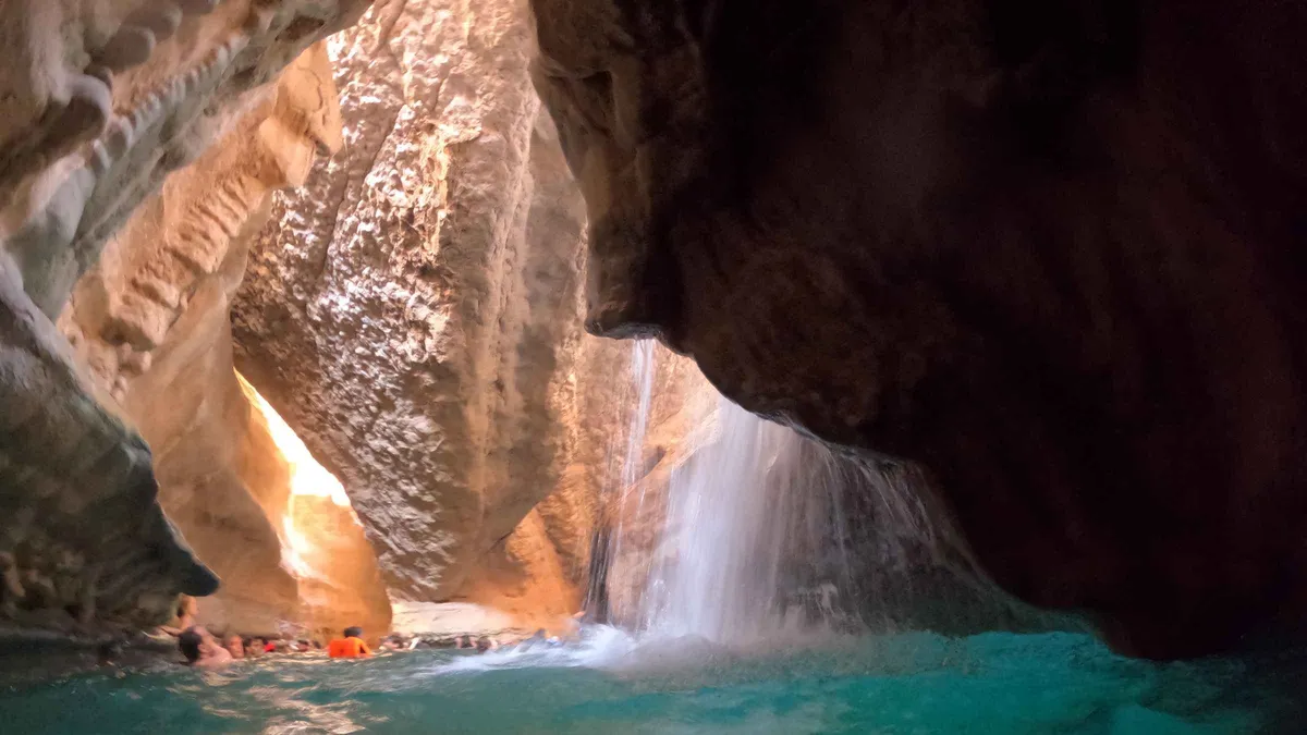 A waterfall pouring into the pool inside the Wadi Shab cave