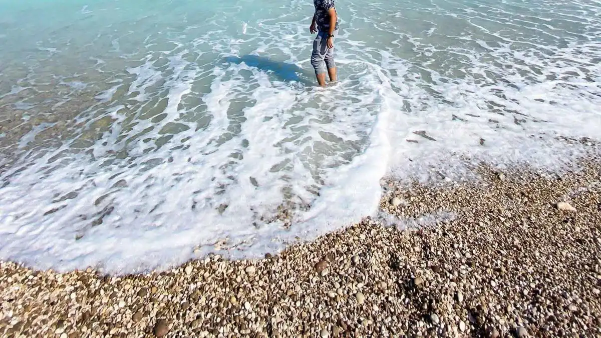 A person standing in the surf on the pebble shore at Fins Beach