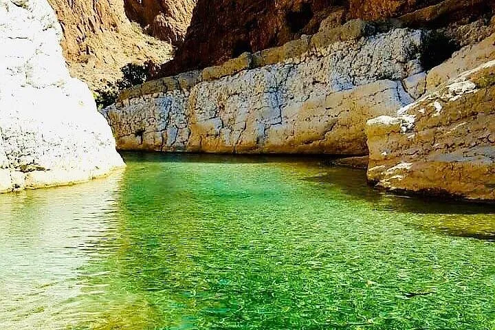 Clear green water under a pale limestone ledge in Wadi Shab