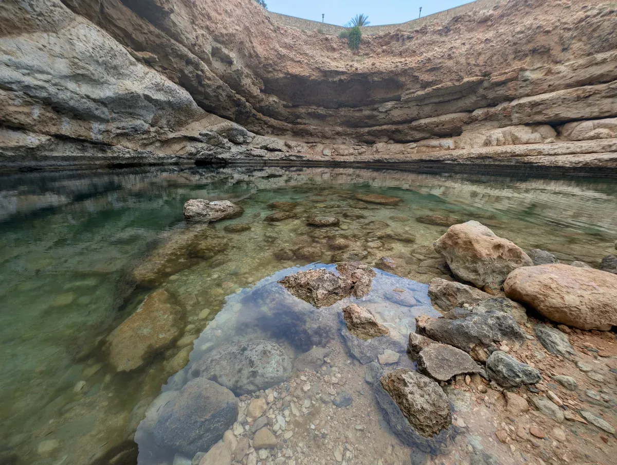 Clear green water and rocks at the bottom of the Bimmah Sinkhole inside its pale limestone rim