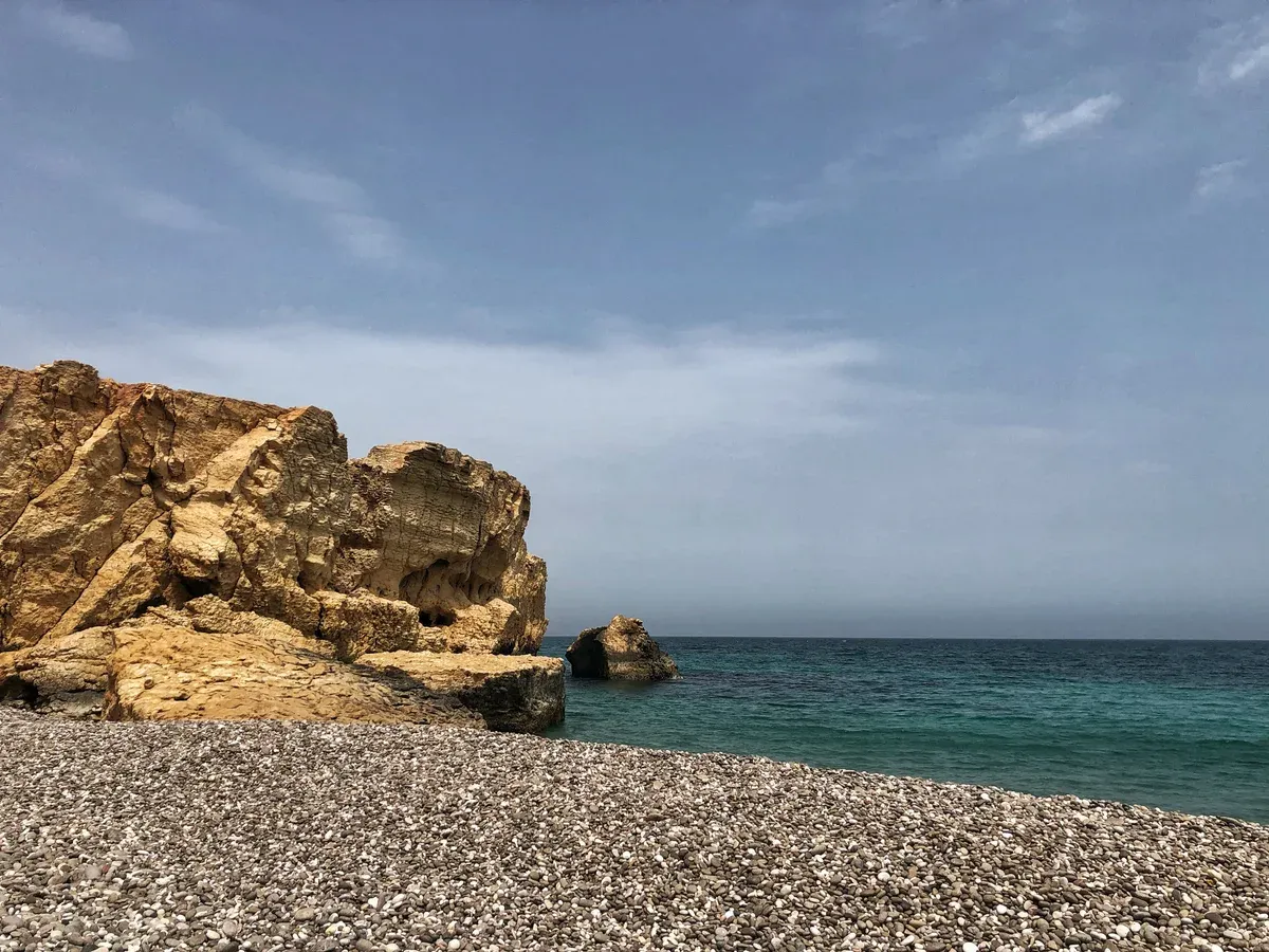 A pebble beach and layered ochre rock on the Gulf of Oman coast near Fins