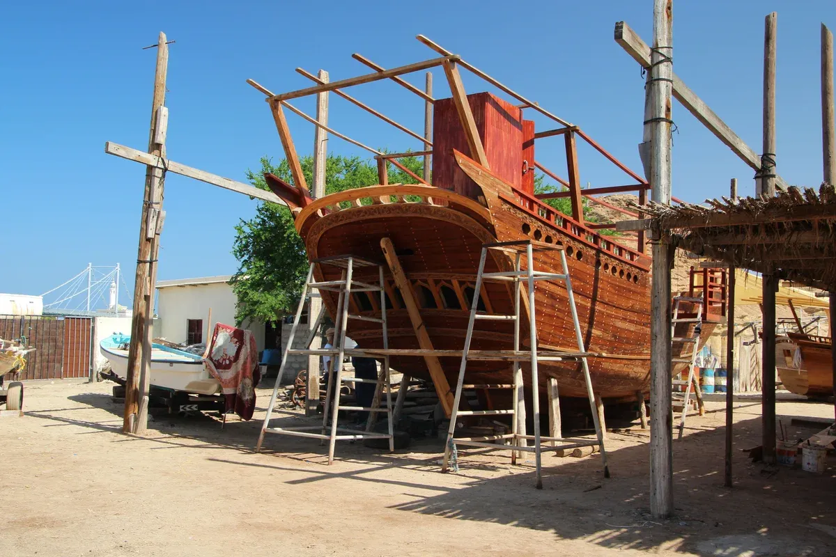 A wooden dhow under construction on scaffolding at the Sur dhow yard